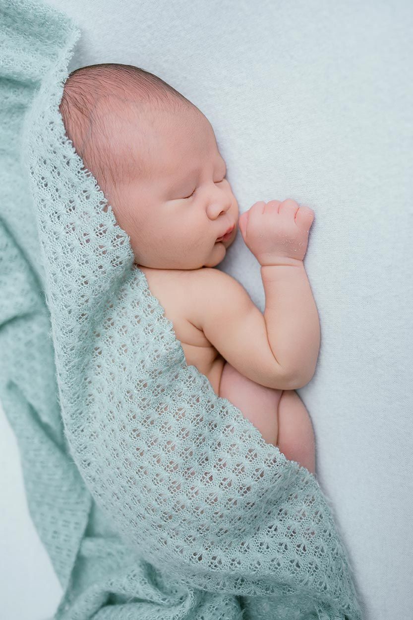 Peaceful newborn baby sleeping wrapped in a soft mint green knit blanket on a light background.