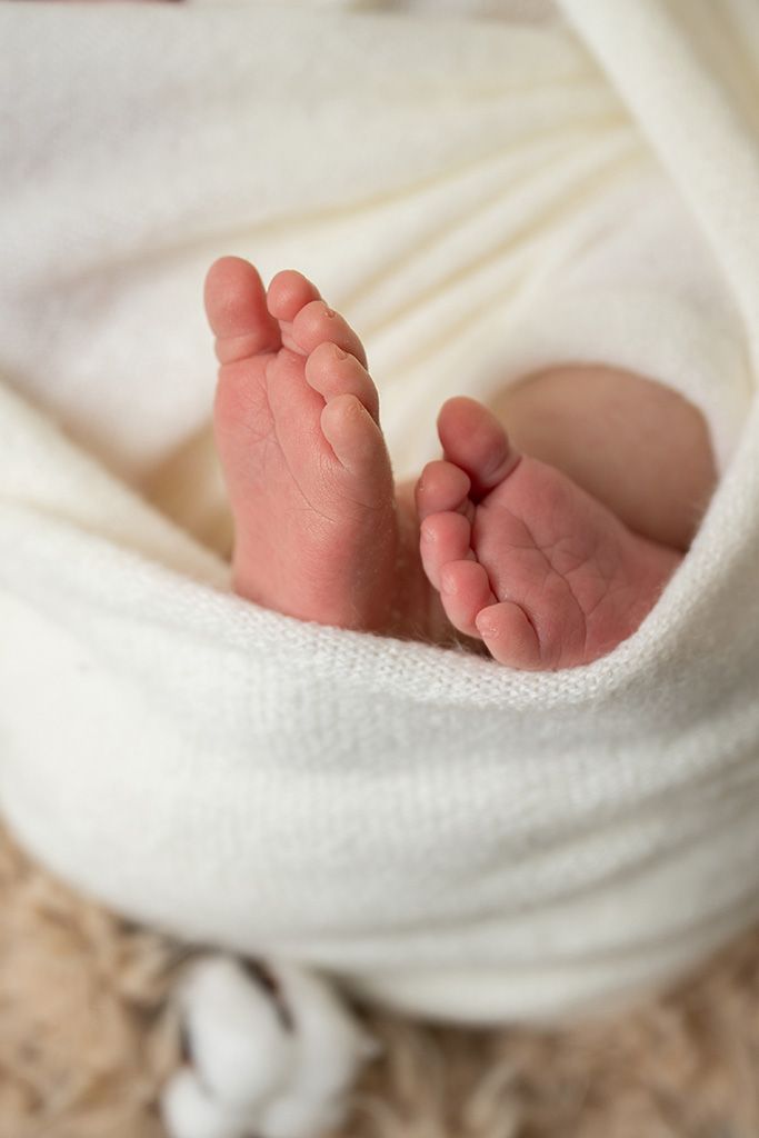 Close-up of tiny newborn baby feet wrapped in a soft white blanket, showcasing delicate toes and skin.