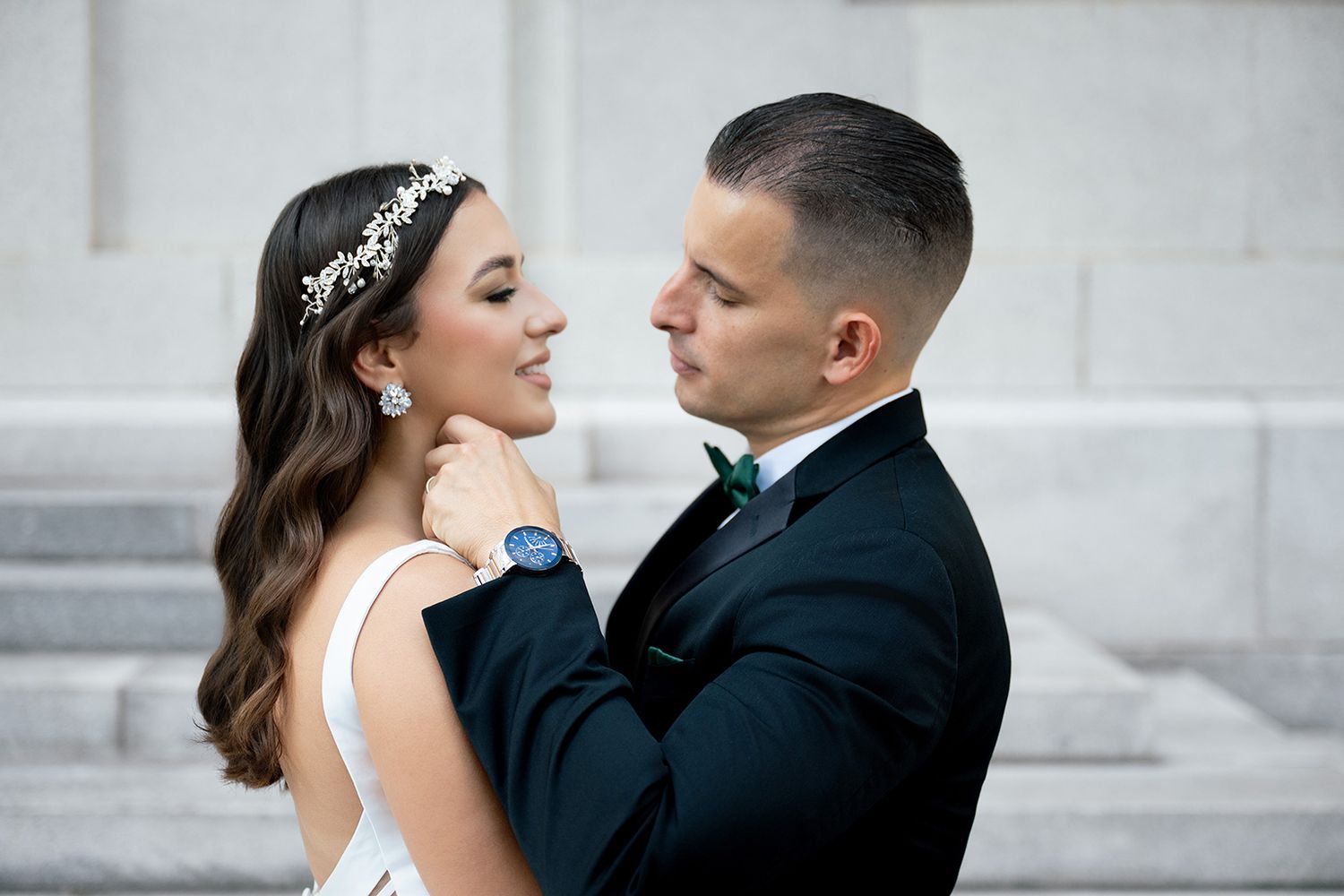 Bride and groom share a romantic moment, she wears a floral crown and pearl earrings.