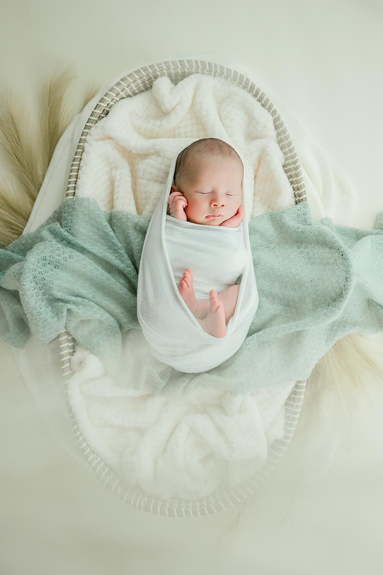 A peaceful sleeping newborn rests in white swaddle on a soft mint green blanket captured from above.