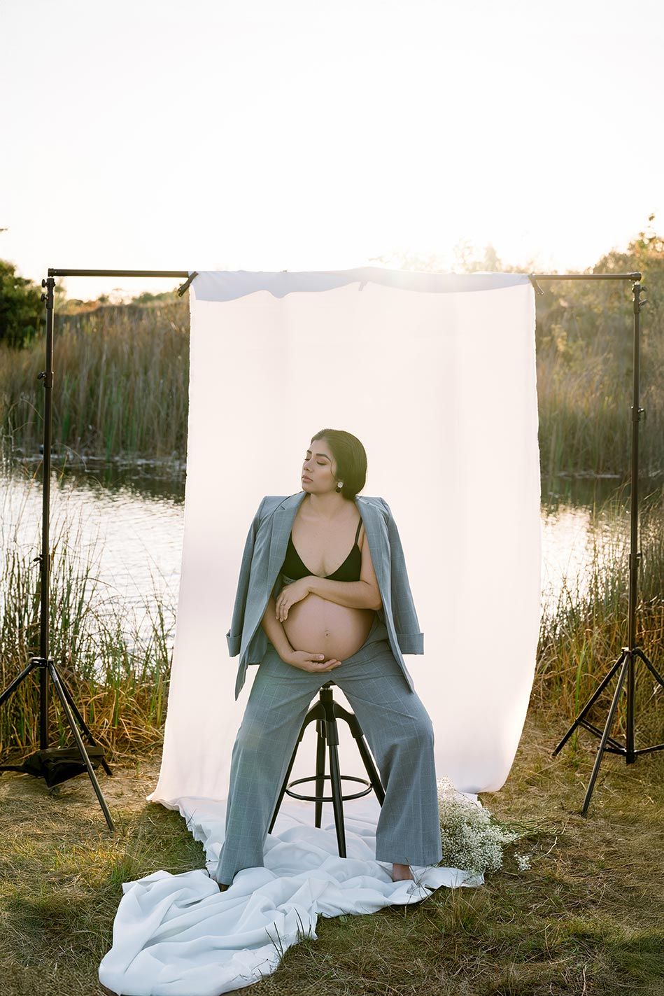 Maternity photo shoot by a lake with white backdrop and studio lights at sunset.