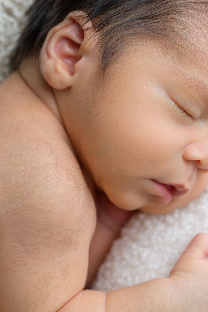 Close-up of a peaceful sleeping newborn baby with dark hair resting on a soft white blanket.