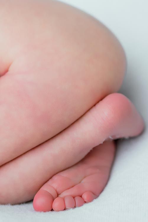 Close-up of a newborn baby's tiny feet and legs on a white blanket.