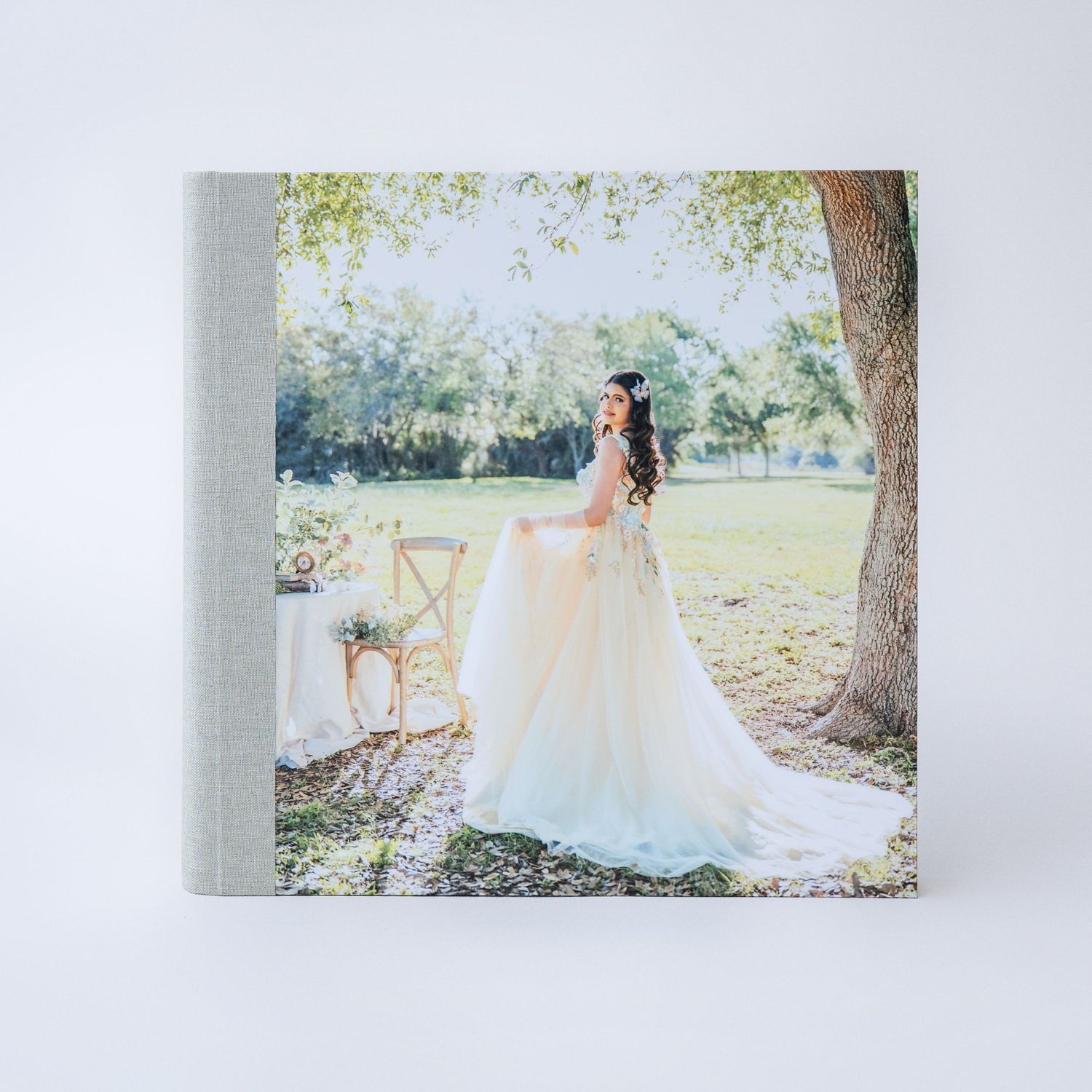 Elegant wedding photo album with a bride in a flowing white gown standing under a tree in a lush garden setting.
