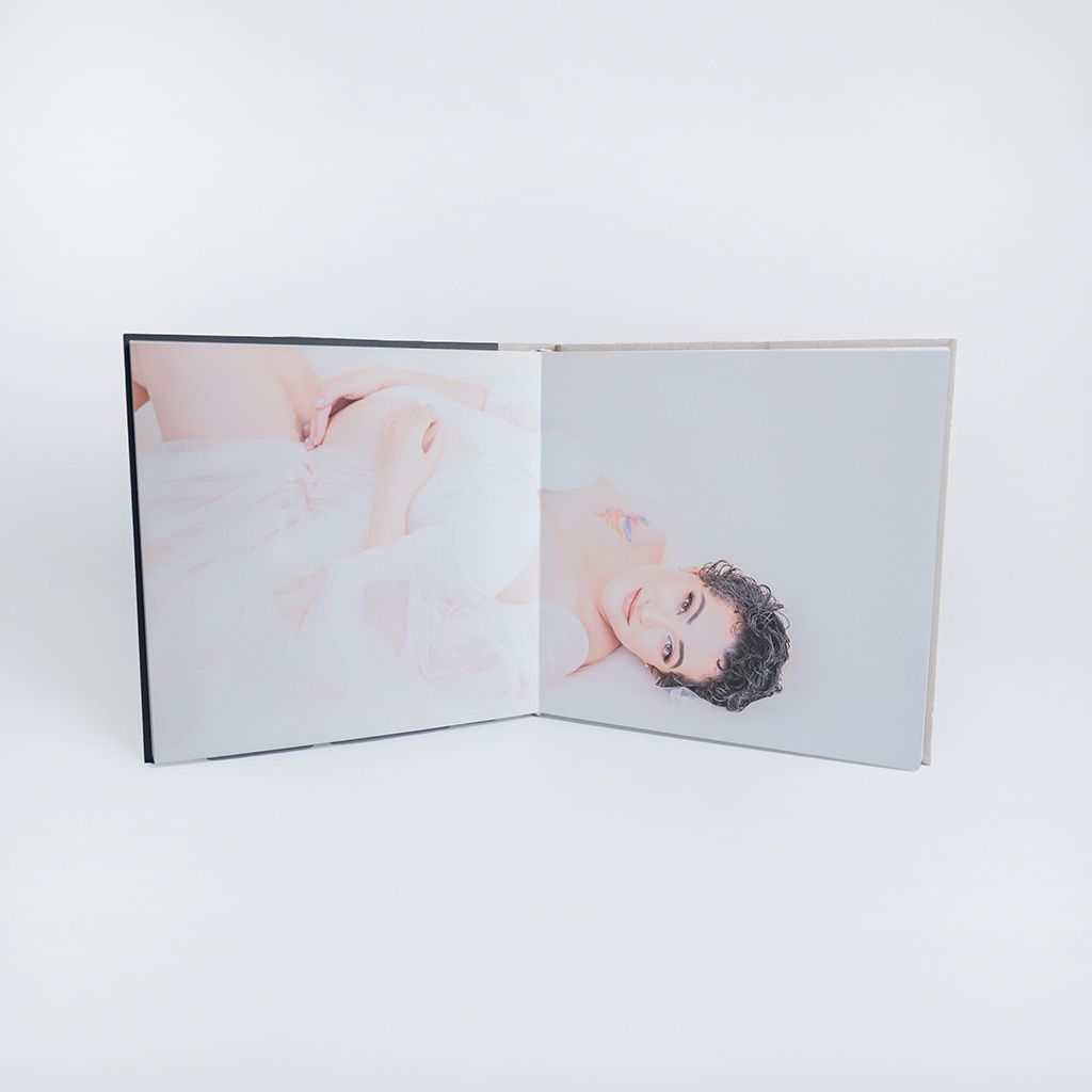 Open photo book displaying soft, dreamy portraits of a young person in white, with a minimalist aesthetic on a white background.