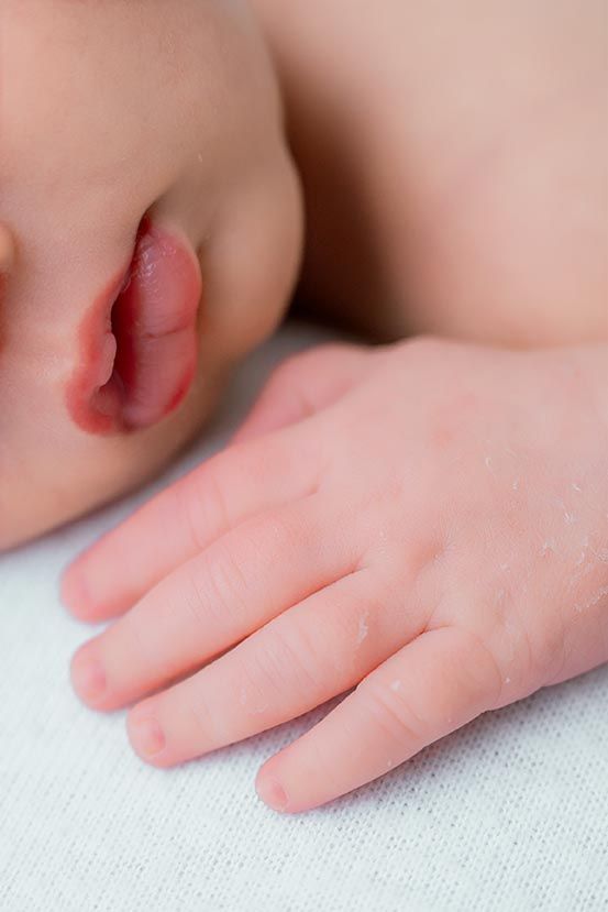 Close-up of a sleeping newborn baby's tiny hand and ear resting on a white surface.