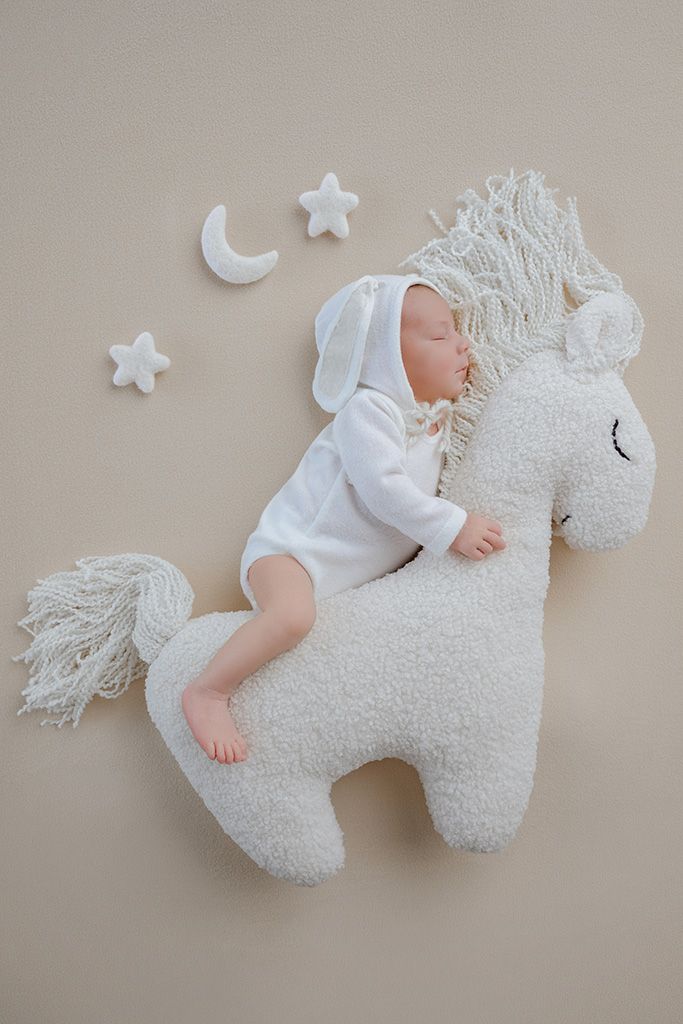 Sleeping newborn baby in white bunny outfit resting on a fluffy unicorn plush toy with moon and stars decor.