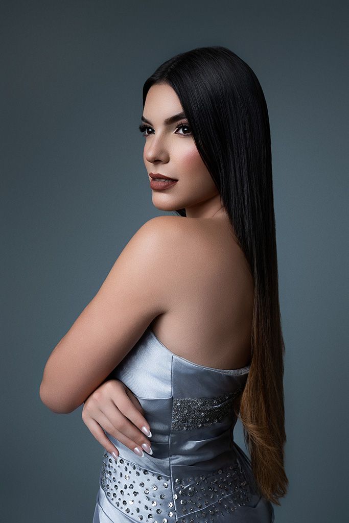 Young woman in strapless silver embellished dress with long dark ombre hair posing in studio.