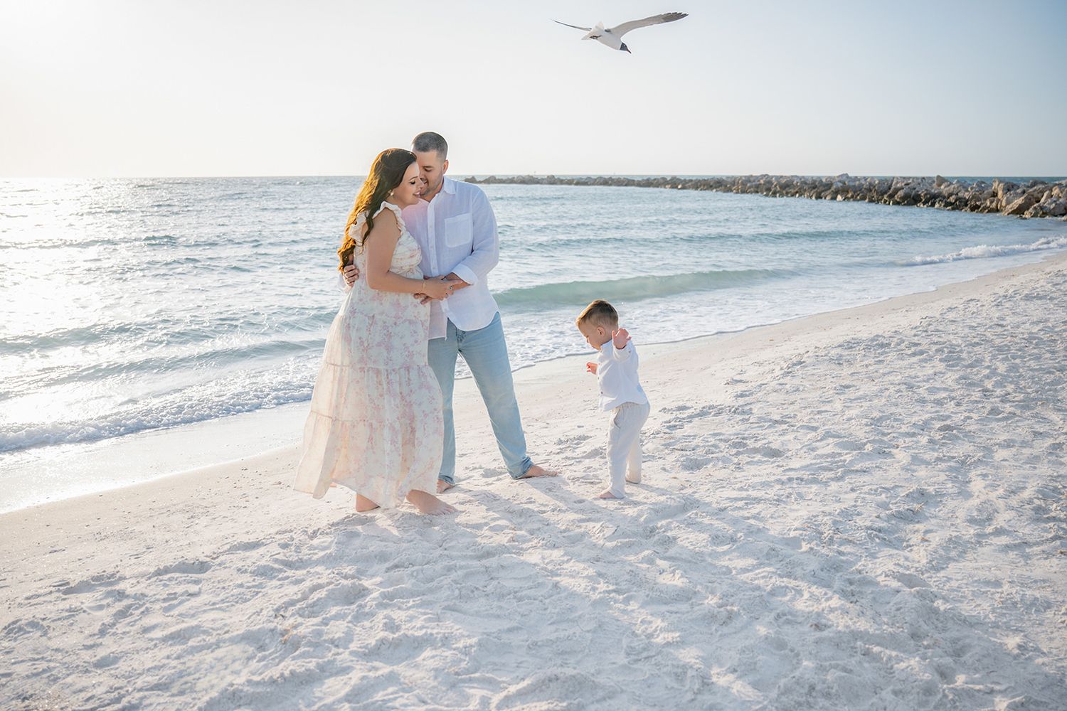 Happy family with toddler enjoying a beautiful beach day by the ocean.