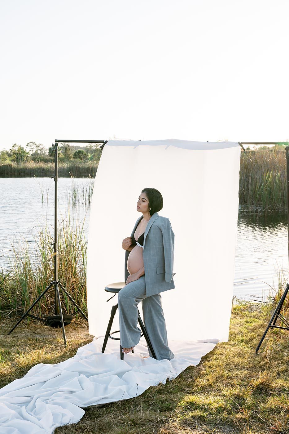 Outdoor photo shoot setup with white backdrop and lighting equipment near a lake with reeds and natural scenery.