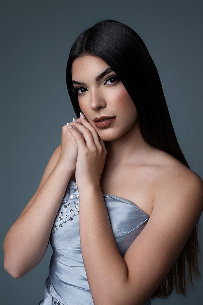 Brunette woman in silver strapless embellished dress posing gracefully against gray background.
