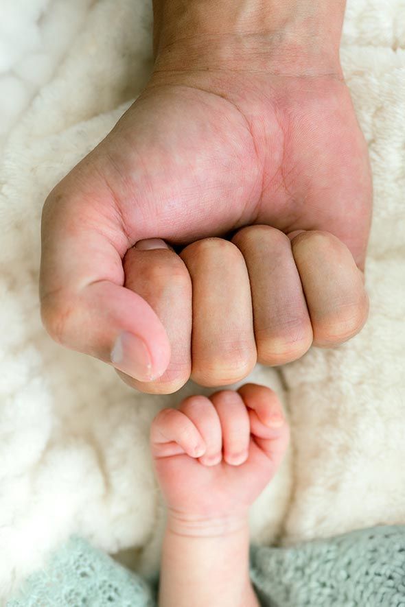 Close-up of a newborn babys tiny hand next to a parents large fist on a soft blanket.