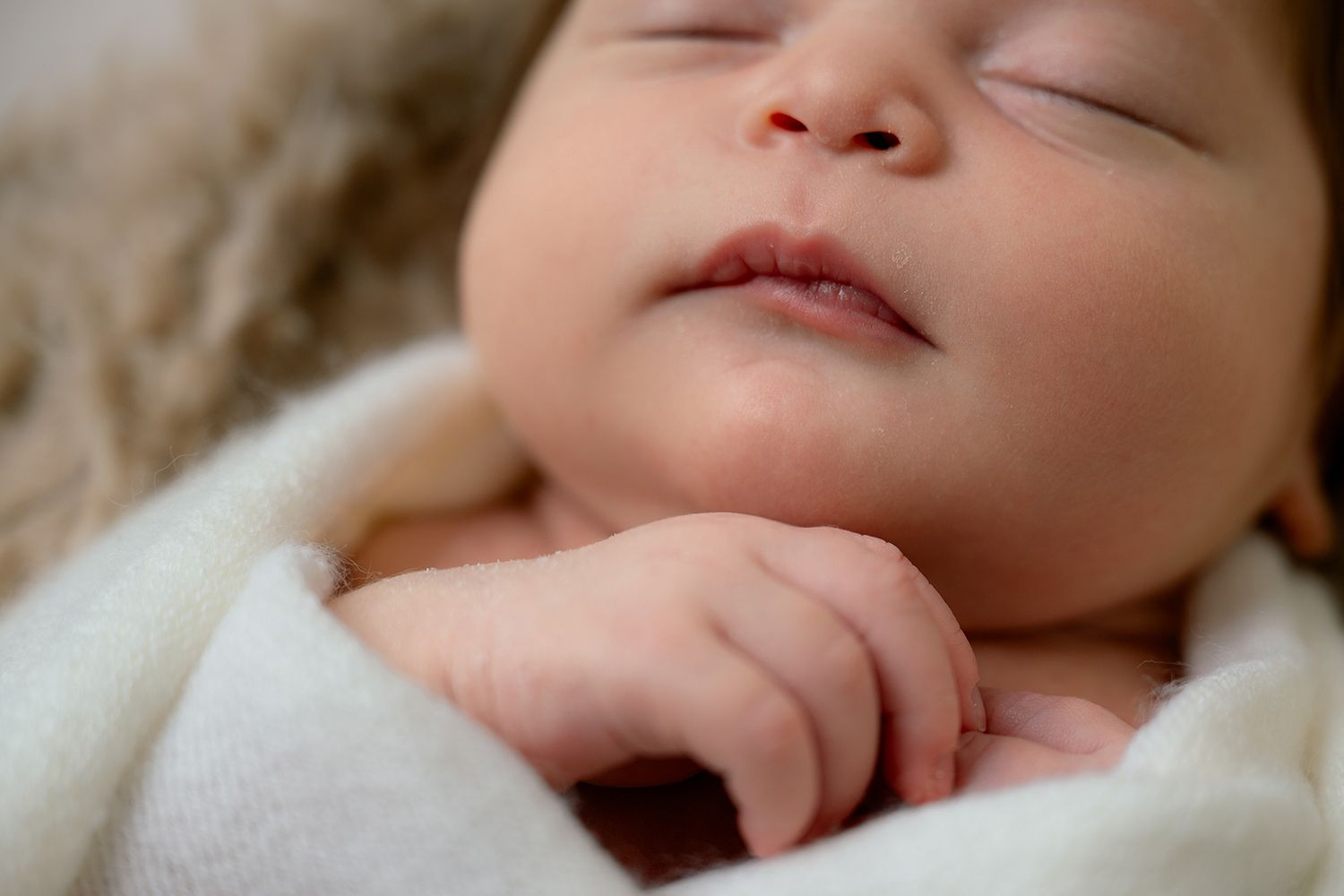 Peaceful newborn baby sleeping soundly wrapped in a soft white blanket with tiny hand visible.