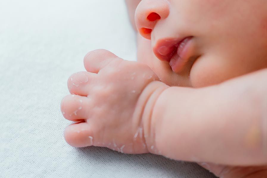 Close-up of a newborn baby's tiny feet and hands resting on a soft white surface.