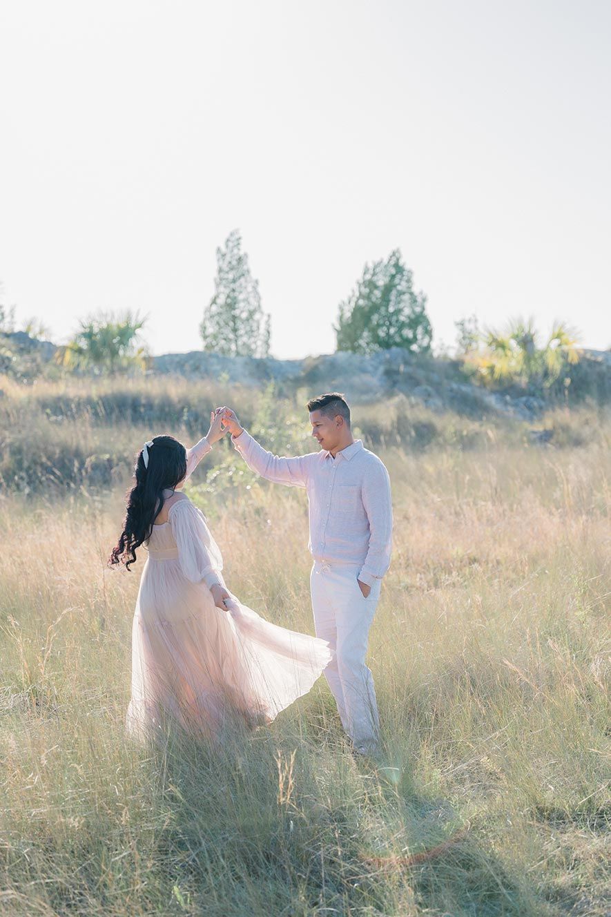 Couple in white outfits standing together in a sunlit meadow during a romantic golden hour photoshoot.