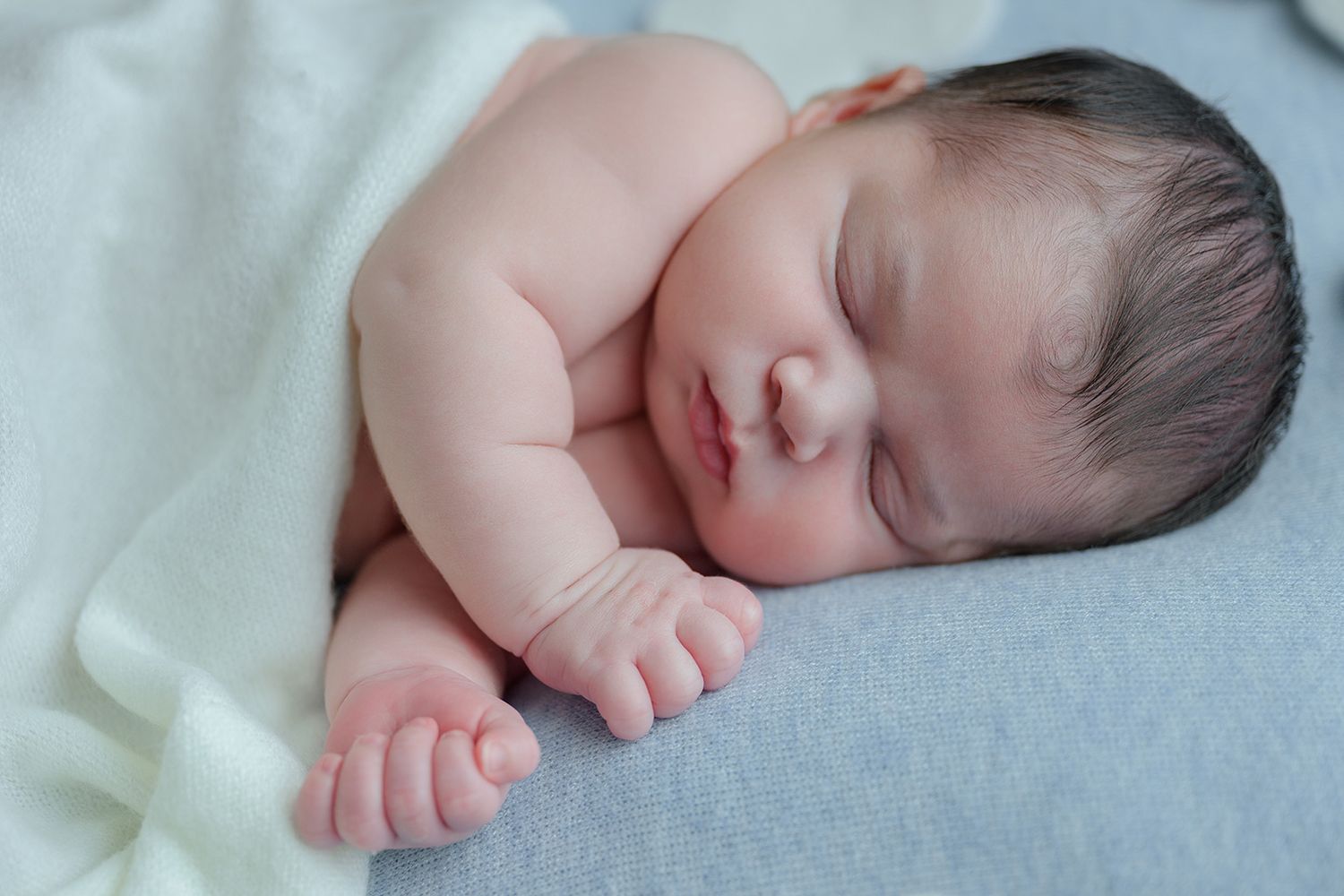 Adorable newborn baby sleeping peacefully on a soft blue blanket wrapped in a white cloth.