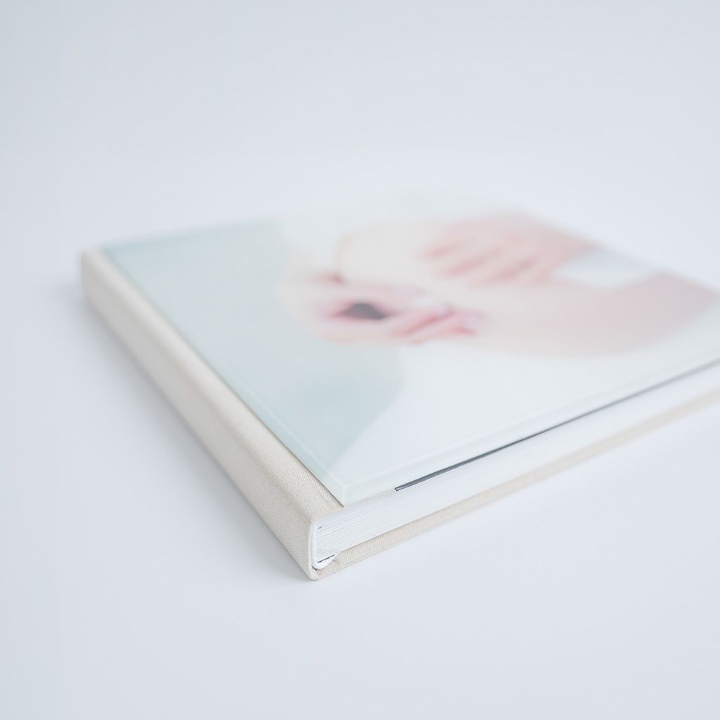 A soft-cover photo book with a delicate pastel image of a baby on the cover, displayed at an angle.