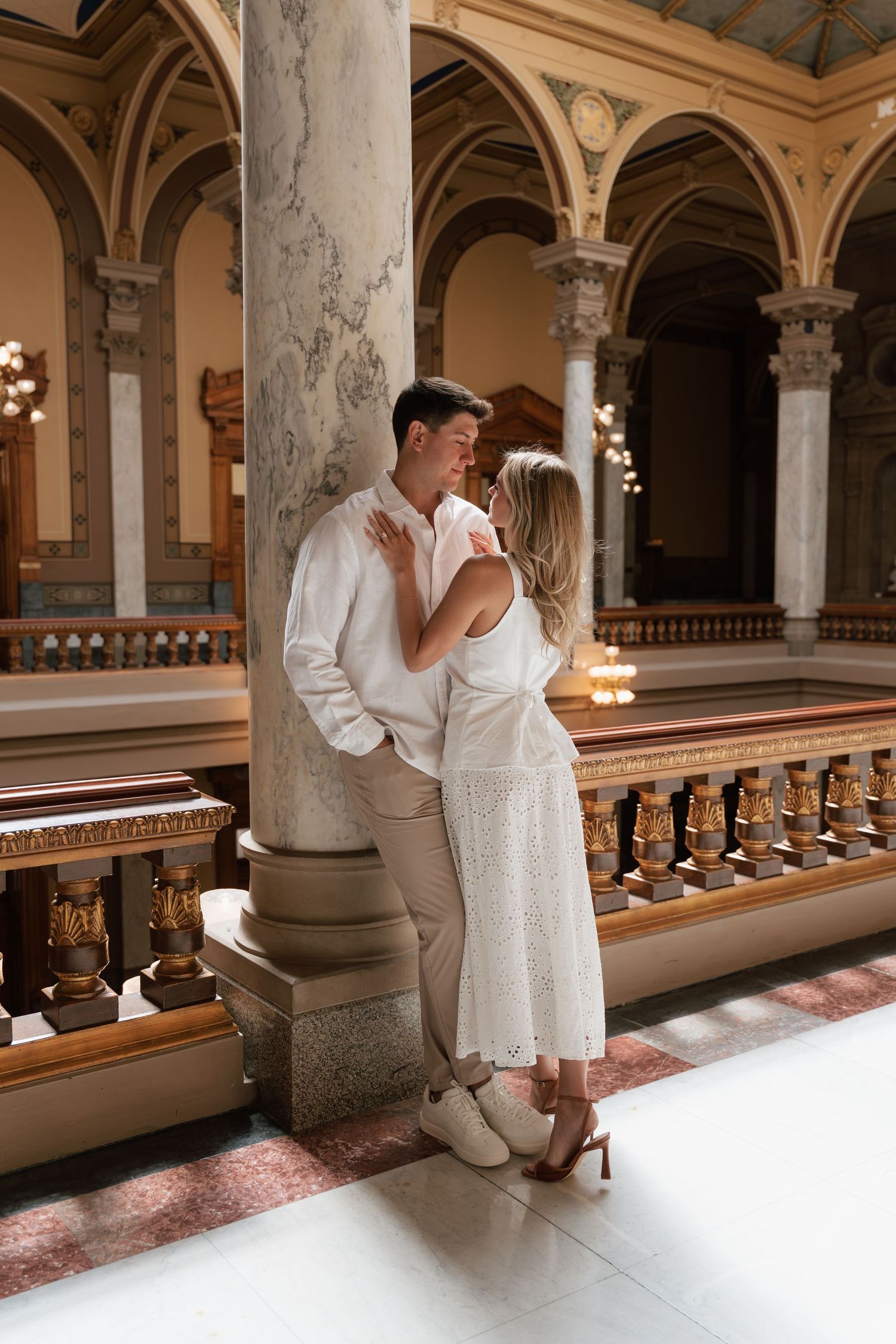Couple sharing a romantic moment leaning against marble column in elegant historic building interior.