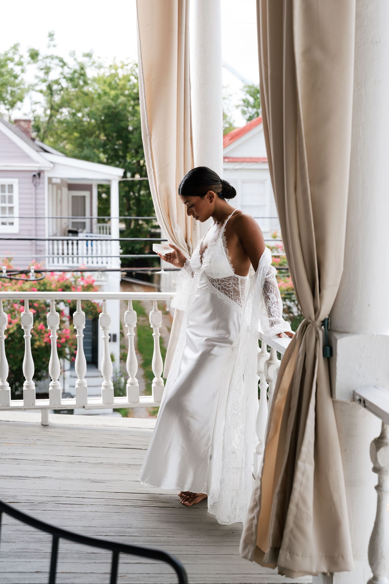 Elegant bride in white backless wedding dress standing on a classic Southern porch with floral backdrop.