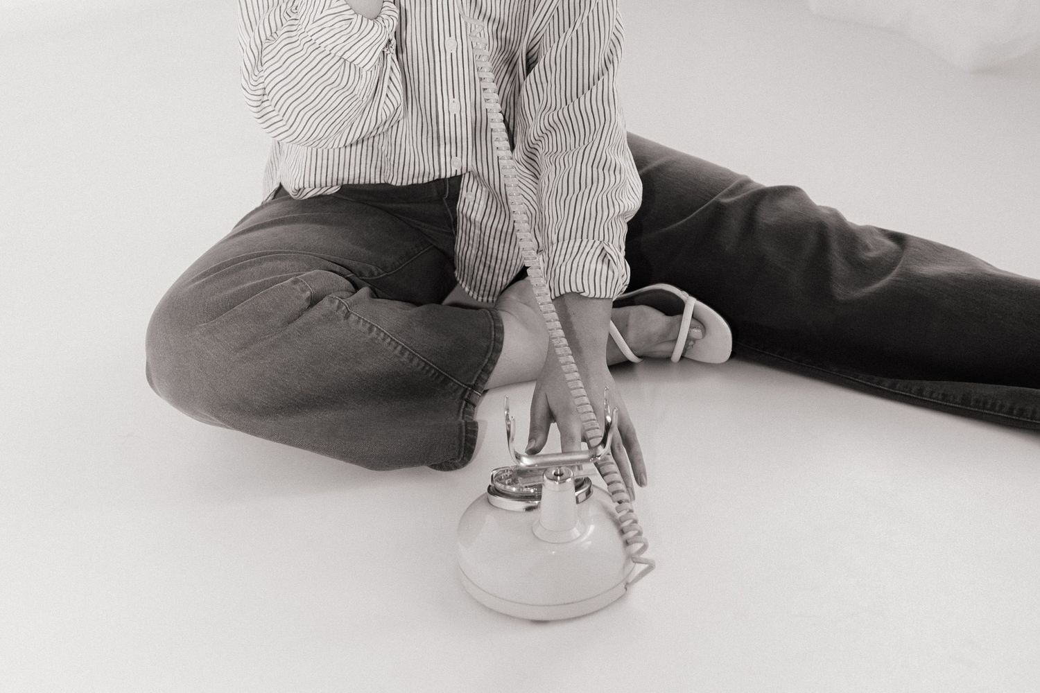 Person sitting on white floor tying shoelaces on white sneakers, wearing striped shirt and dark gray pants.