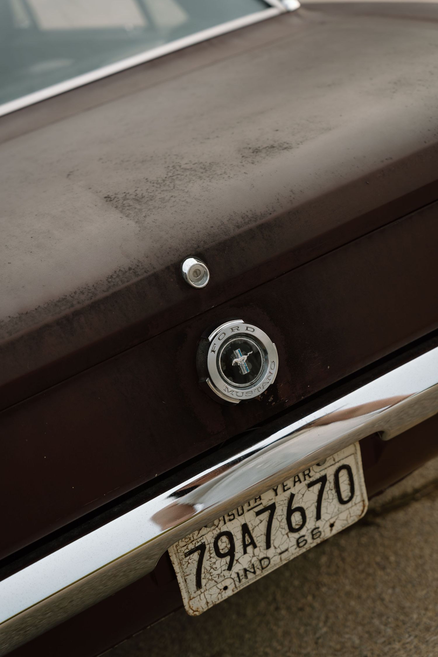 Rear view of a vintage Ford Mustang with Indiana license plate 79A7670, showing dusty trunk and chrome bumper.