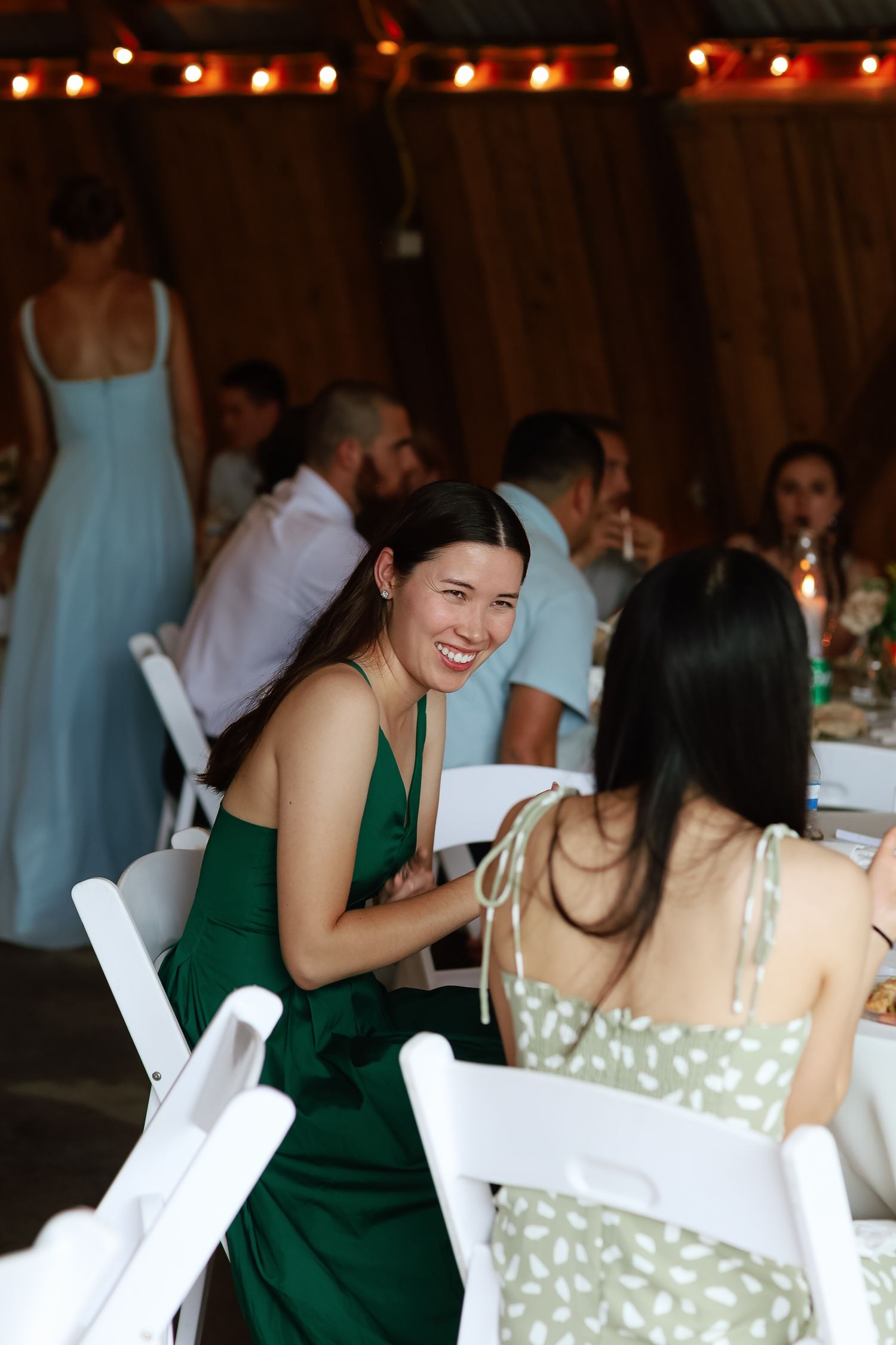 Woman in green dress laughing at wedding reception table inside decorated barn venue.