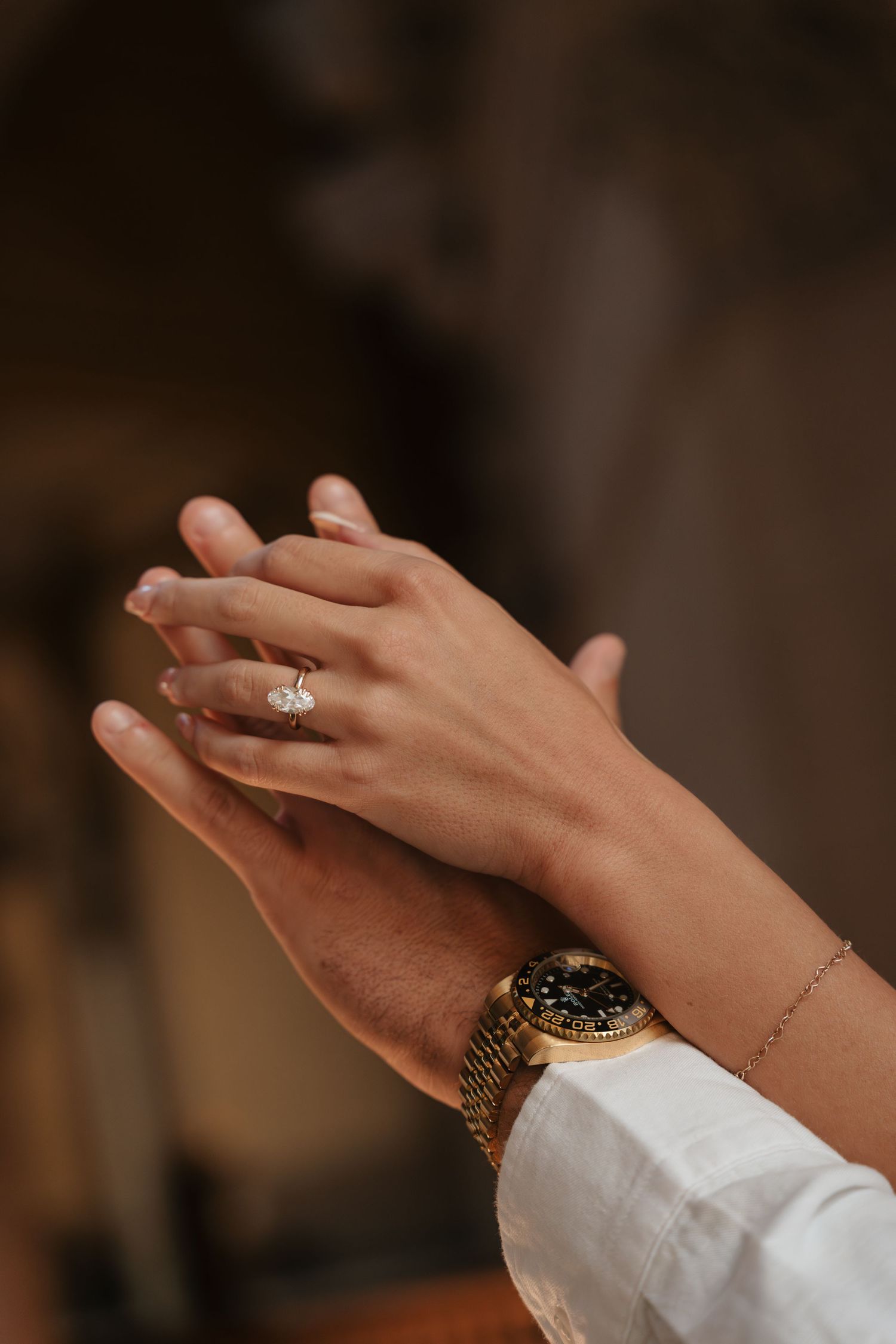 Close-up of couple's hands, woman wearing diamond engagement ring, man wearing gold Rolex watch.