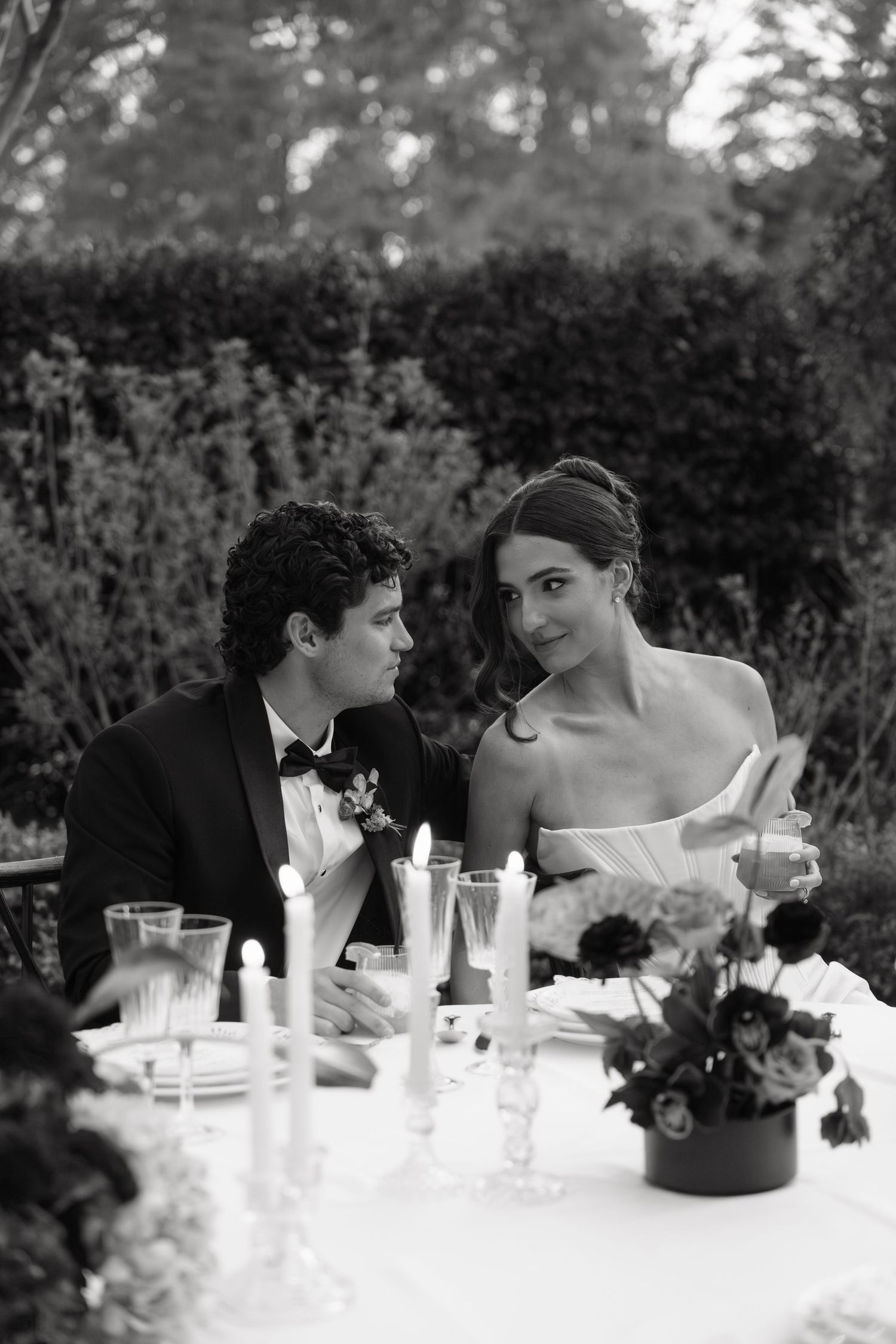 Black and white photo of a bride and groom sharing an intimate moment at a candlelit outdoor wedding reception table.
