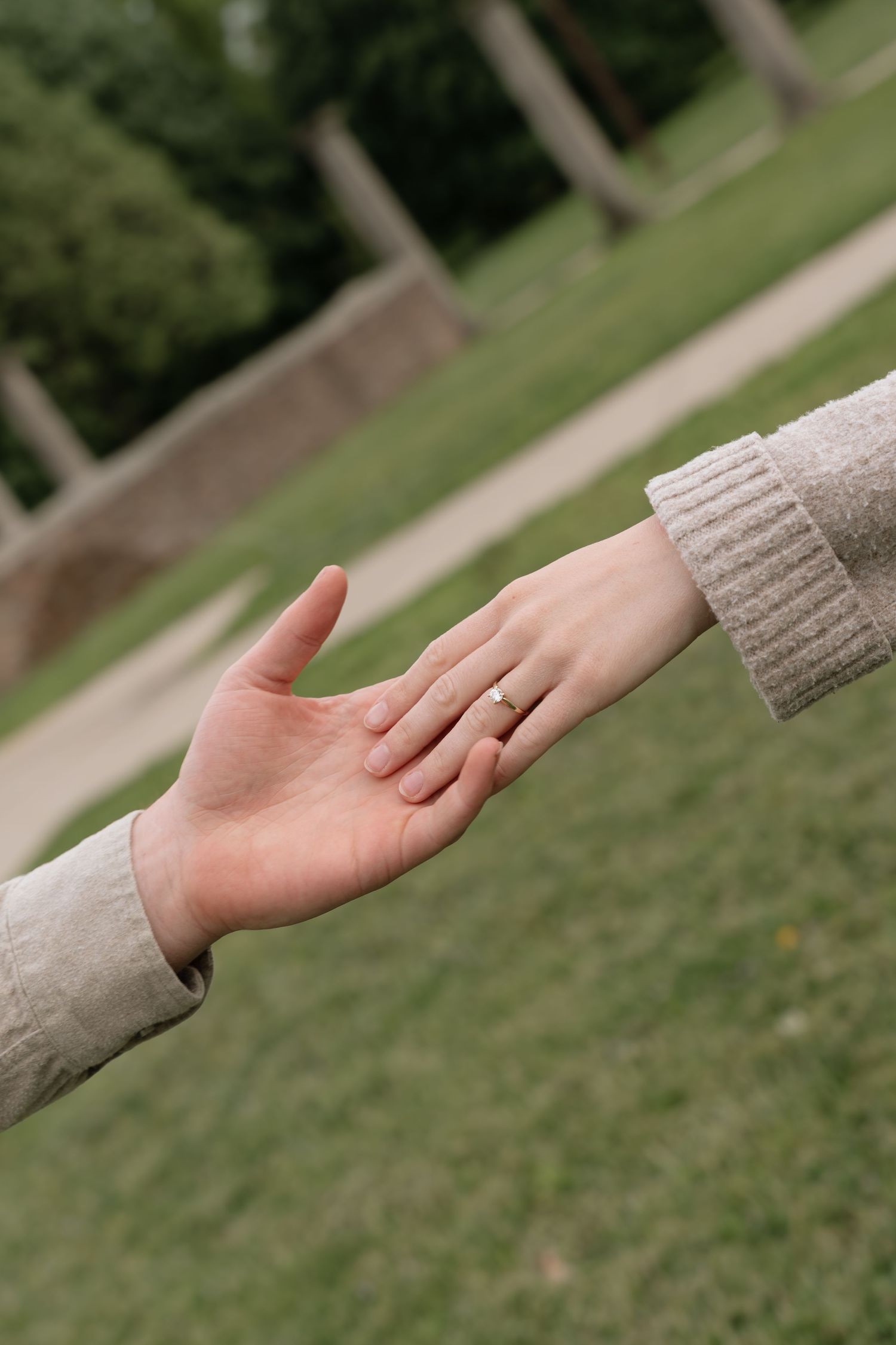 Two hands reaching toward each other outdoors, one wearing an engagement ring, symbolizing love and commitment.
