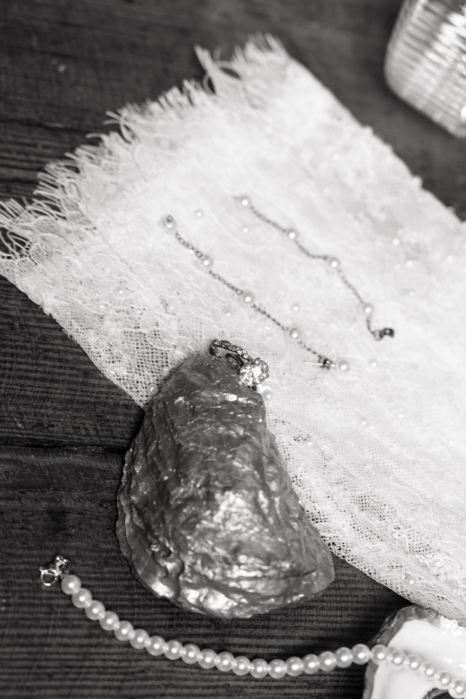 Black and white flat lay of pearl necklace, drop earrings, and oyster shell on white lace fabric.