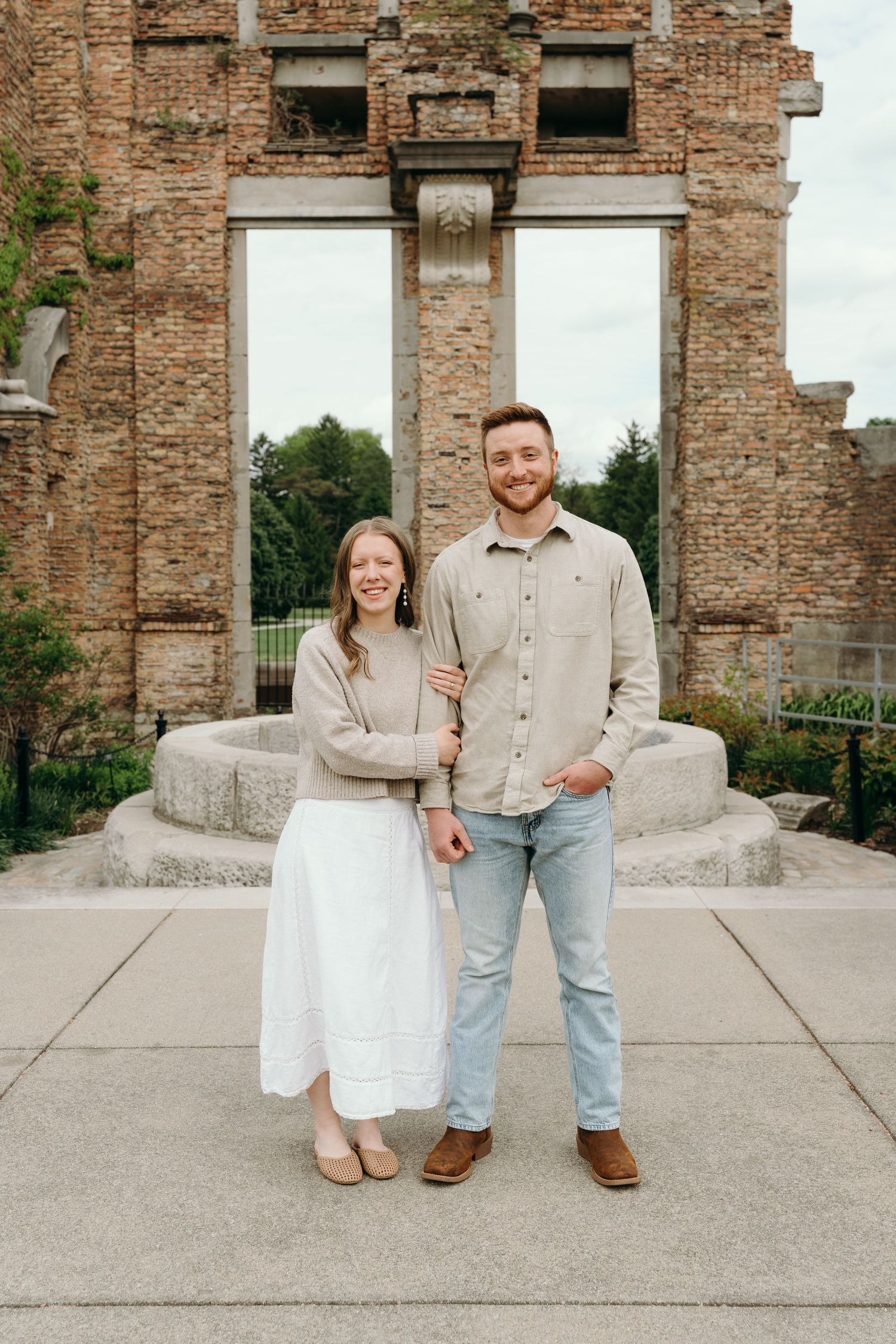 Couple smiling together in front of historic brick ruins and stone fountain outdoors.