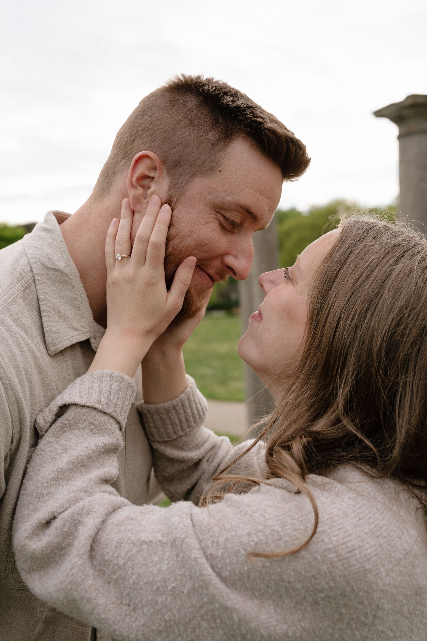A couple shares a tender moment, with a woman cradling a man's face as they lean in for a kiss outdoors.