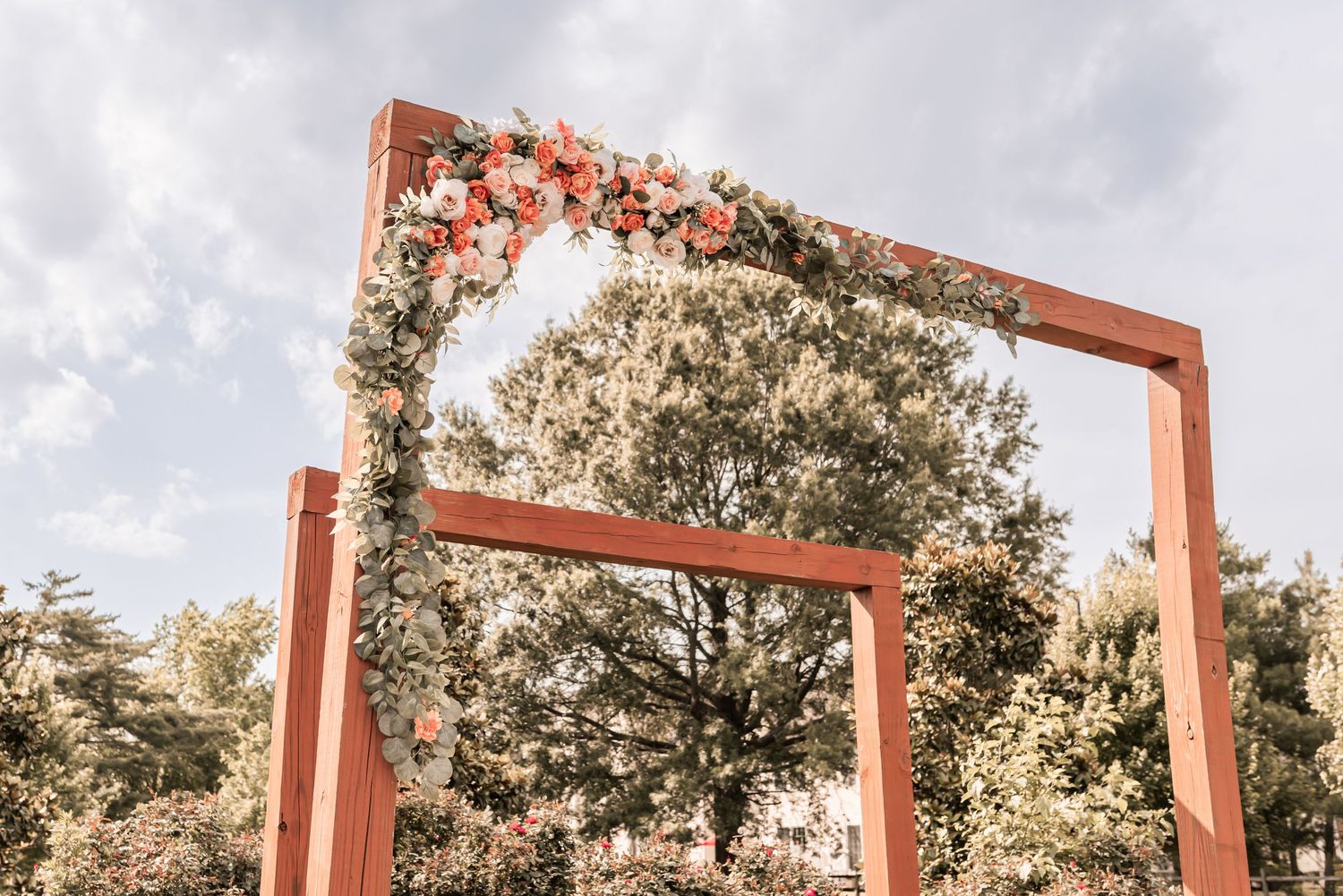 Row of rustic orange metal frames stand against cloudy sky with trees in background creating architectural interest.