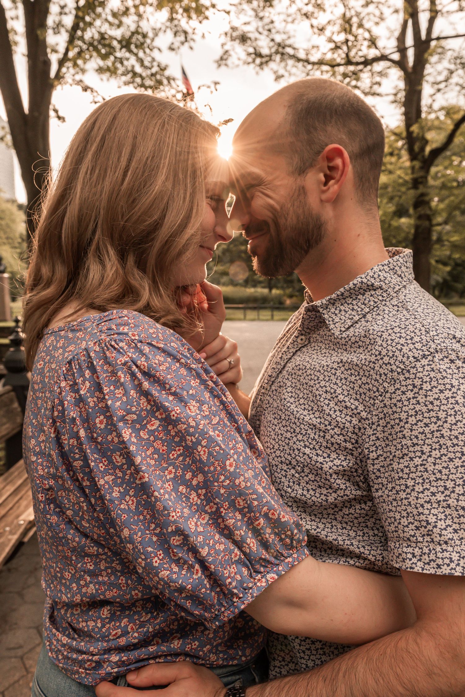 A couple shares an intimate moment outdoors during golden hour sunset, dressed in floral and patterned shirts.