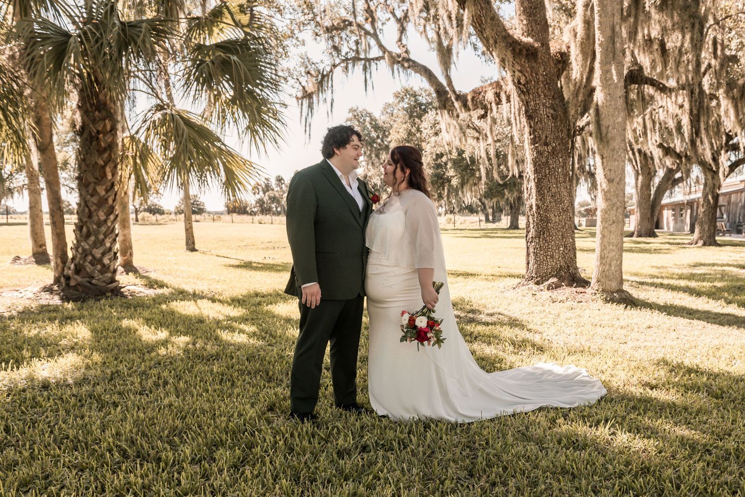 A couple shares an intimate moment under Spanish moss-draped trees in a romantic outdoor wedding setting.
