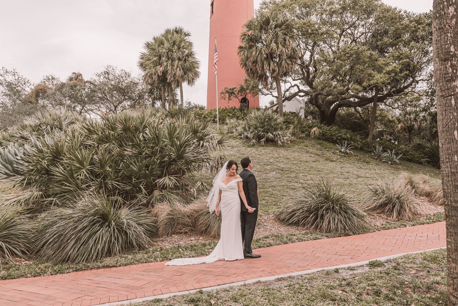 Couple embraces on a pink pathway surrounded by tropical landscaping and palm trees at a pink-hued resort.