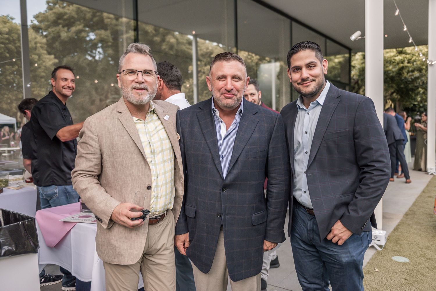 A group of well-dressed people in business attire and suits gather outdoors at a social event.