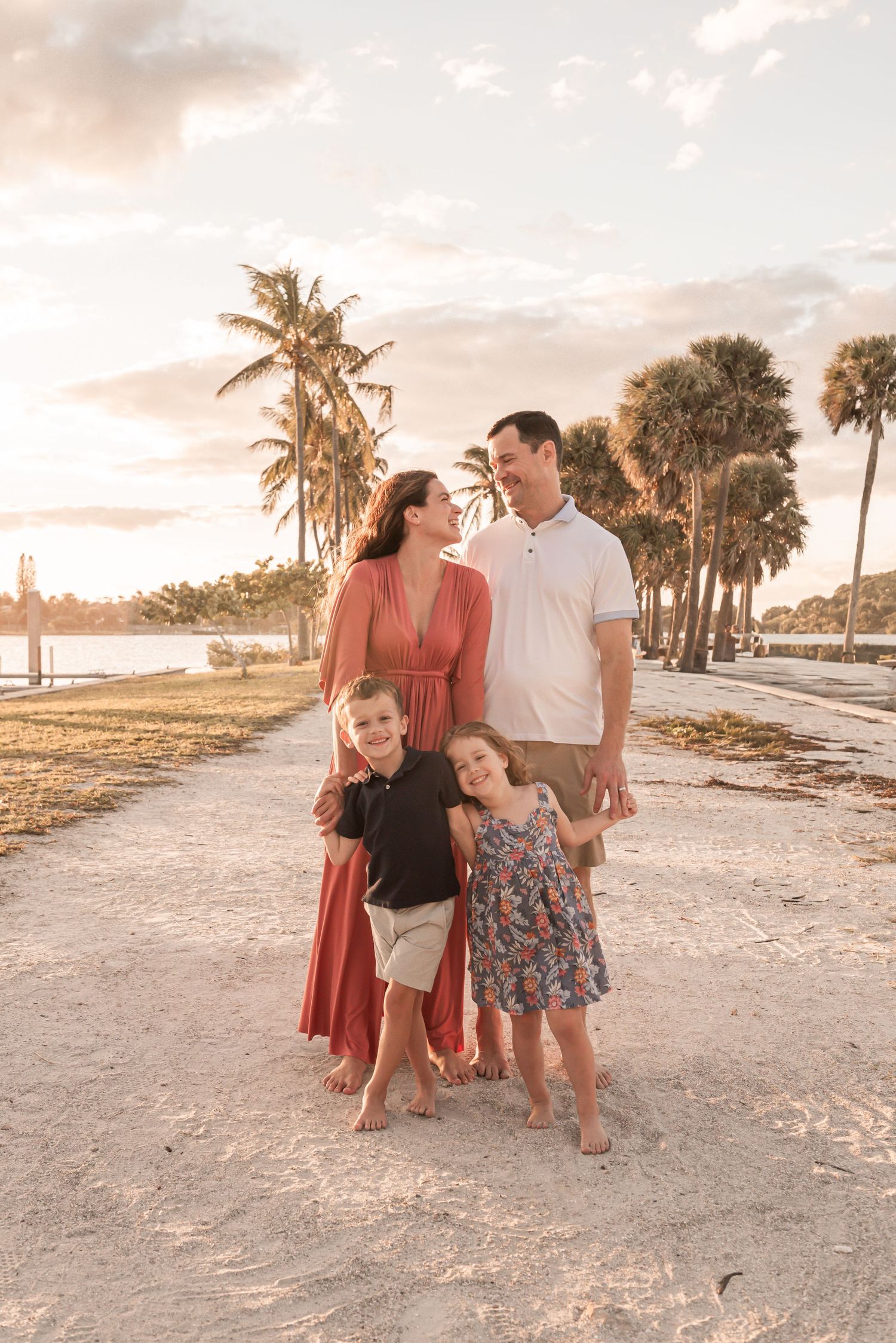 Family enjoying sunset together on sandy beach with palm trees in warm golden light.