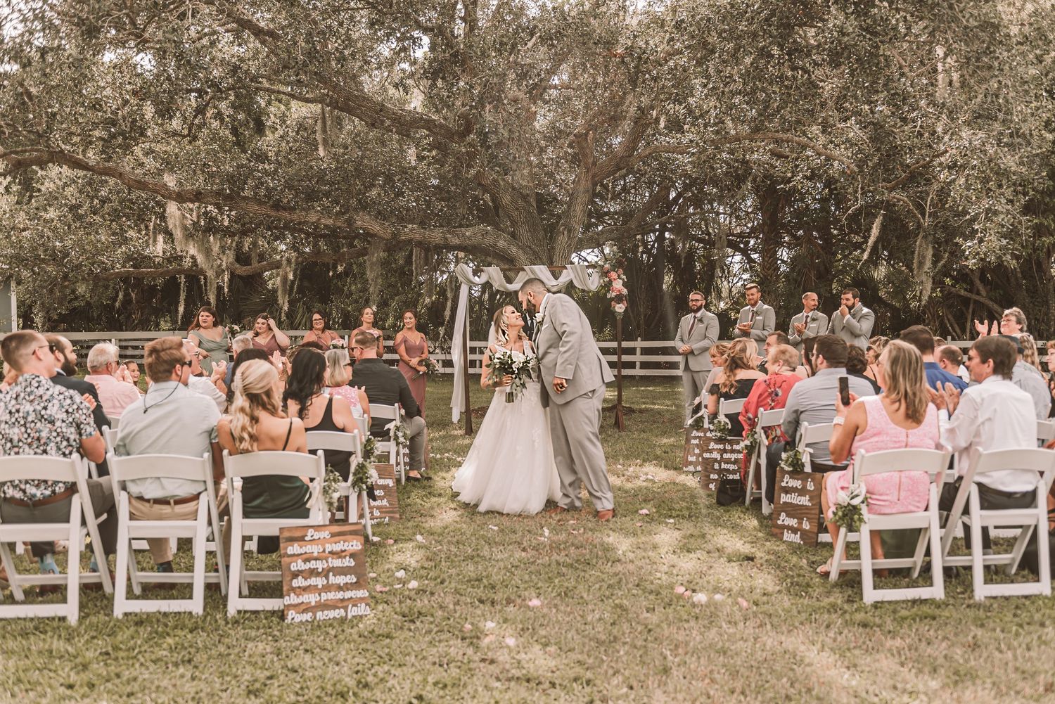 Wedding guests seated in white chairs on a lawn during an outdoor garden ceremony.