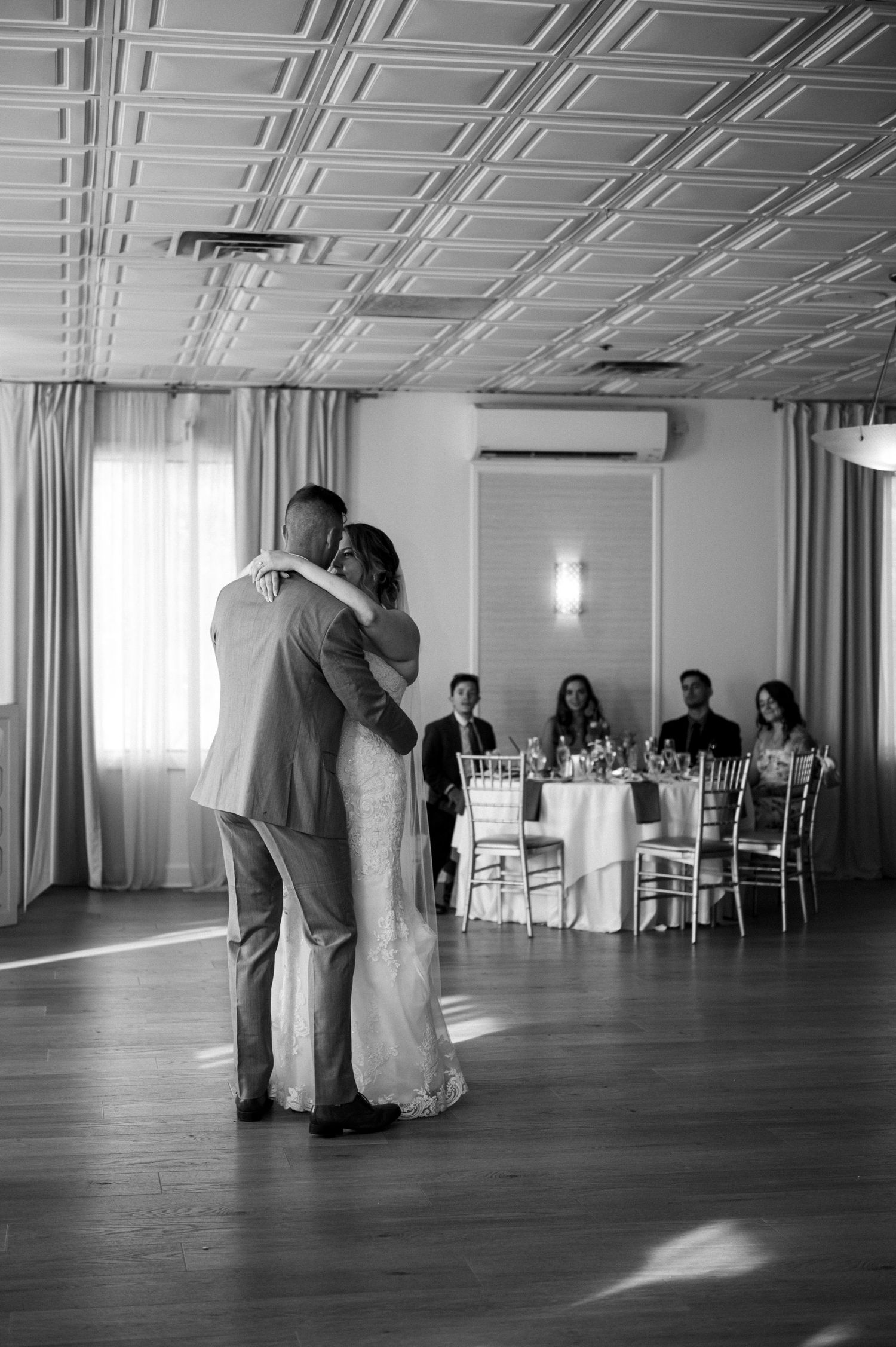 A romantic first dance moment in an elegant ballroom with guests watching from dining tables.