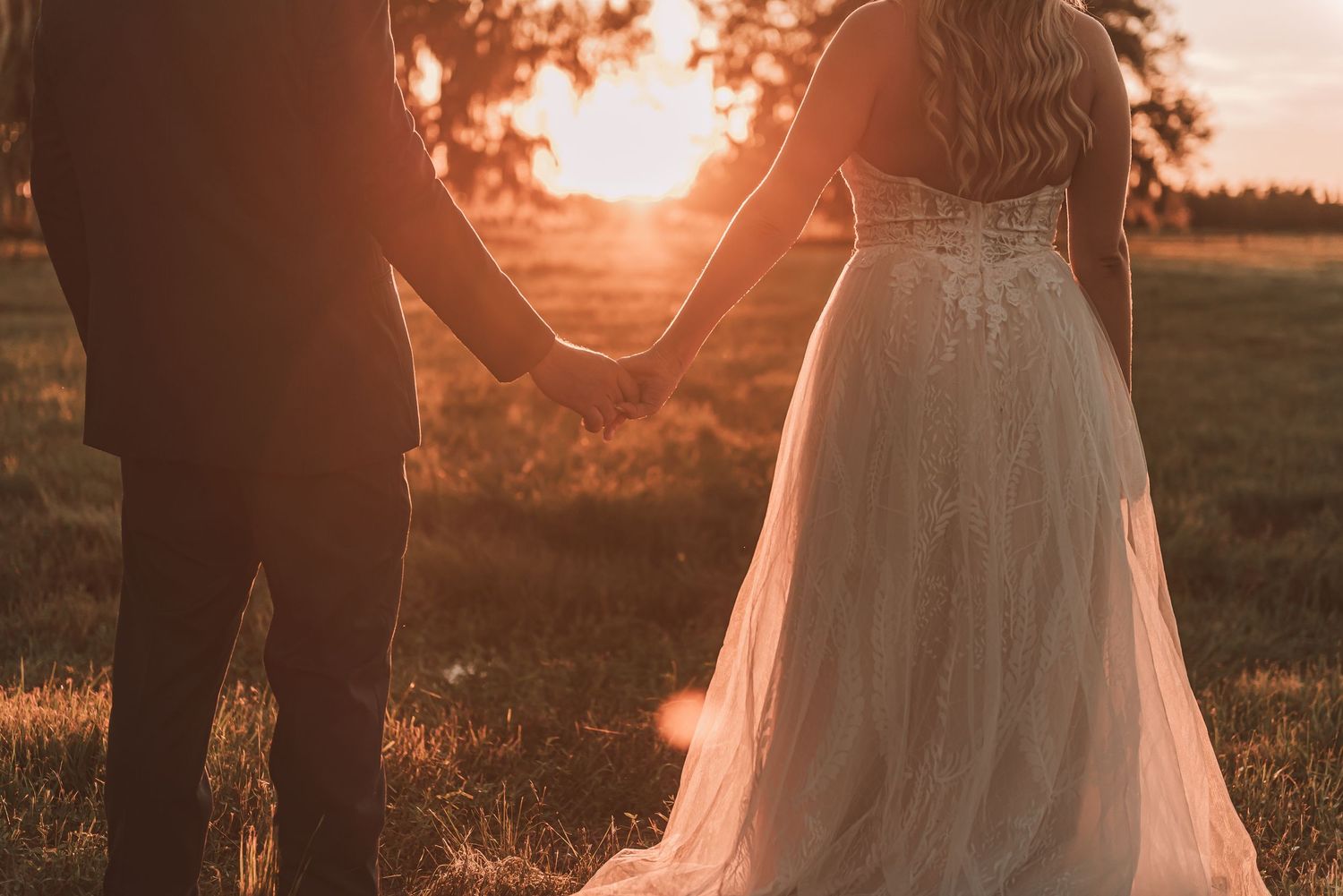 Romantic sunset silhouettes against a warm orange sky as couple stands together in a grassy field.