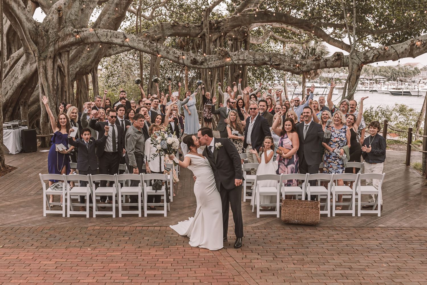 Outdoor wedding ceremony setup with white chairs arranged in rows under rustic wooden beams and natural lighting.