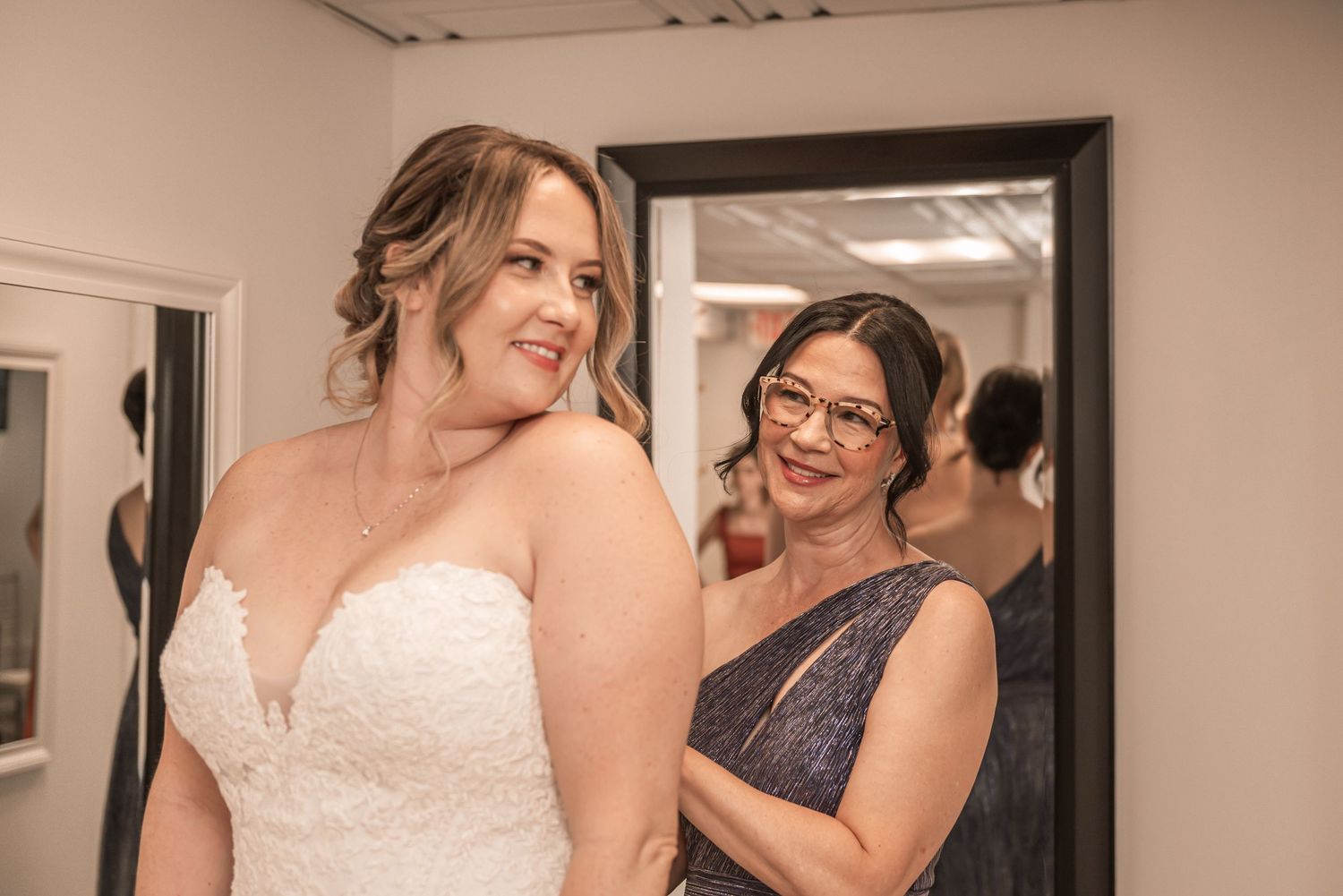 Two people share an intimate moment in a dressing room while getting ready for a formal event.