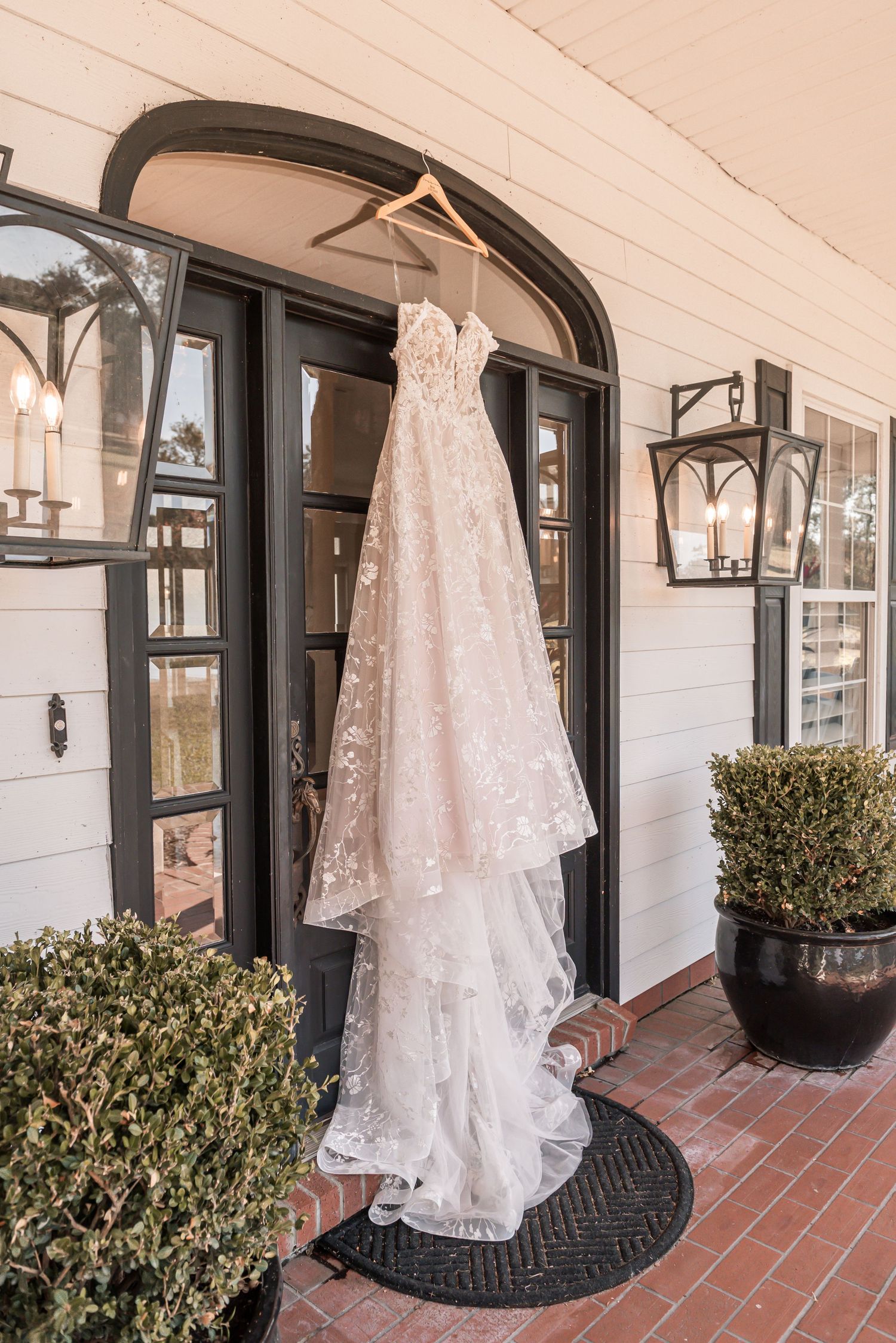 White lace wedding dress hangs elegantly on a porch with black trim and terracotta tiles.