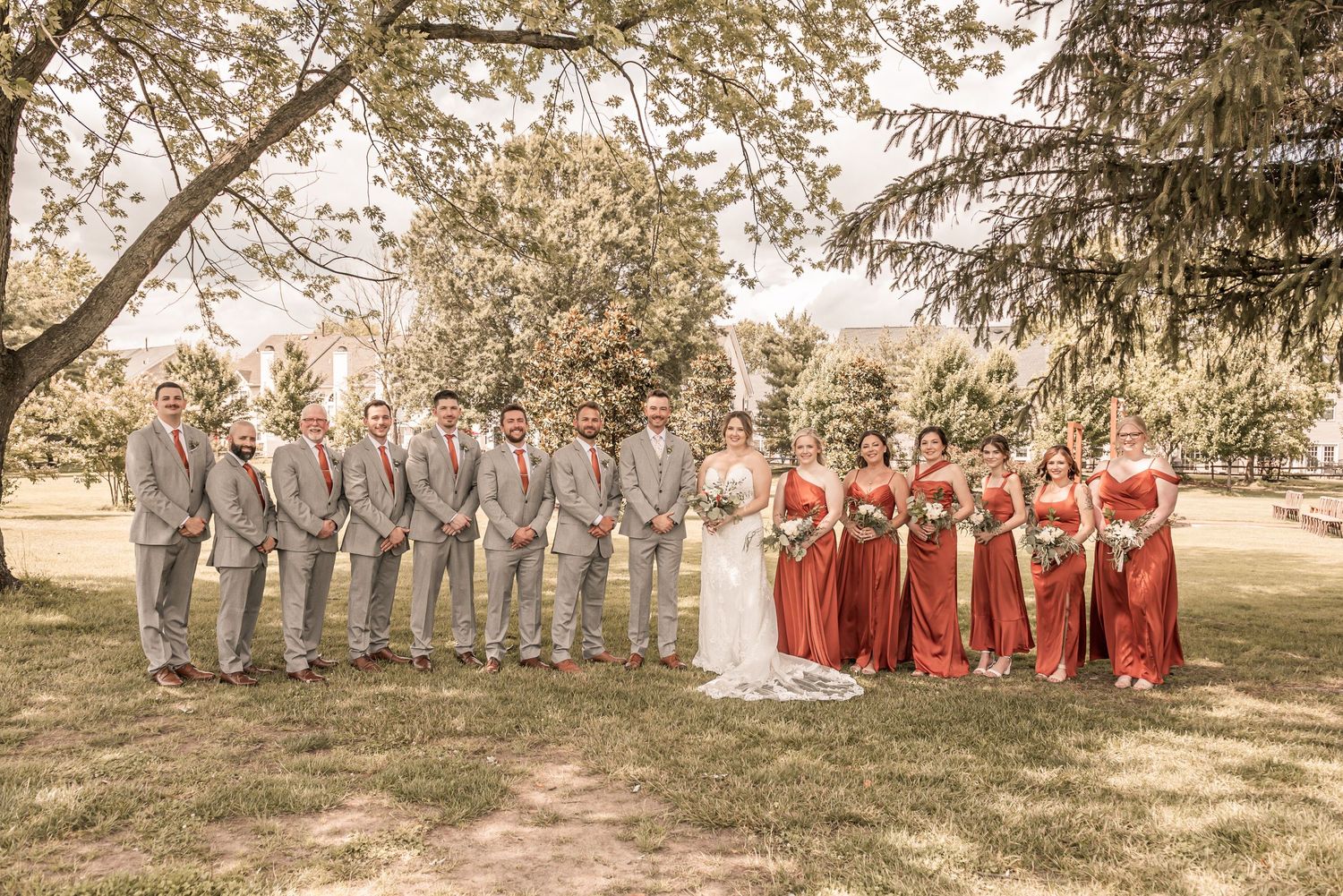 Wedding party members in red and gray dresses stand together in a line outdoors during a fall ceremony.