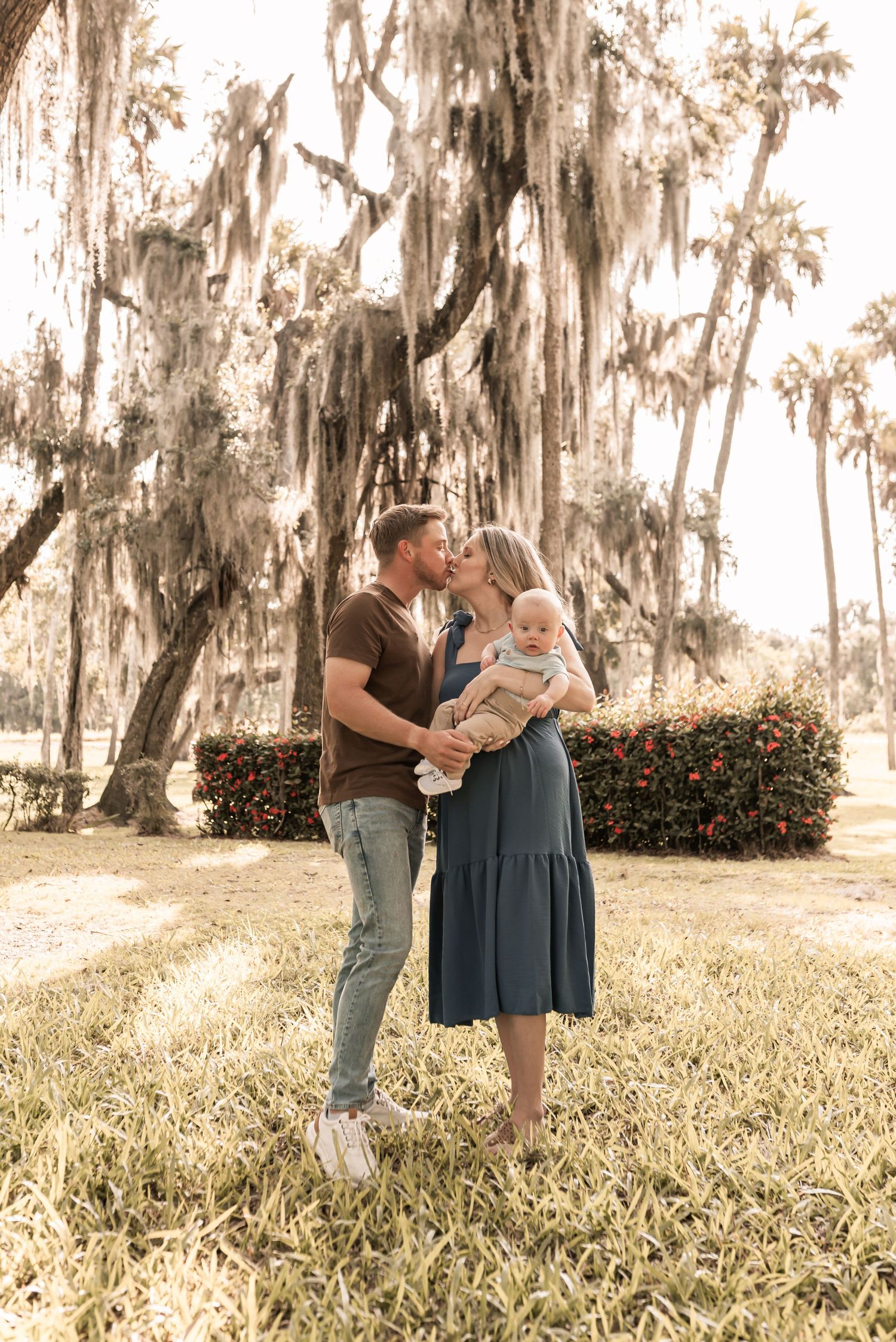 Family sharing a tender moment outdoors against a backdrop of Spanish moss-draped trees in soft golden light.
