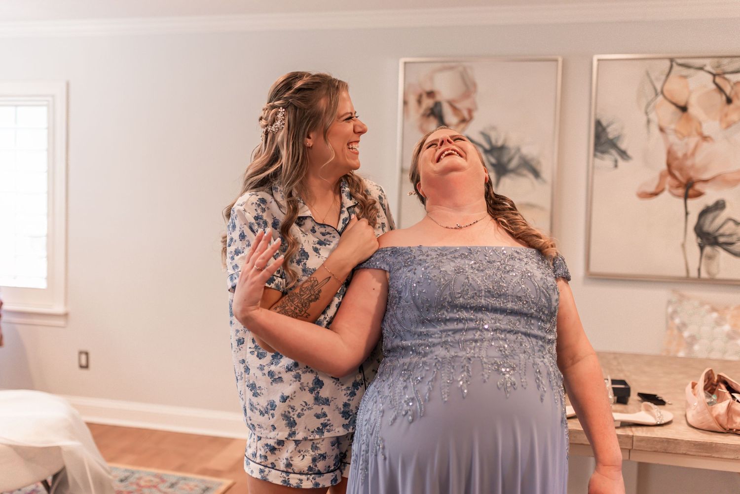 Two people in coordinating gray and floral dresses share an emotional moment during a special occasion.