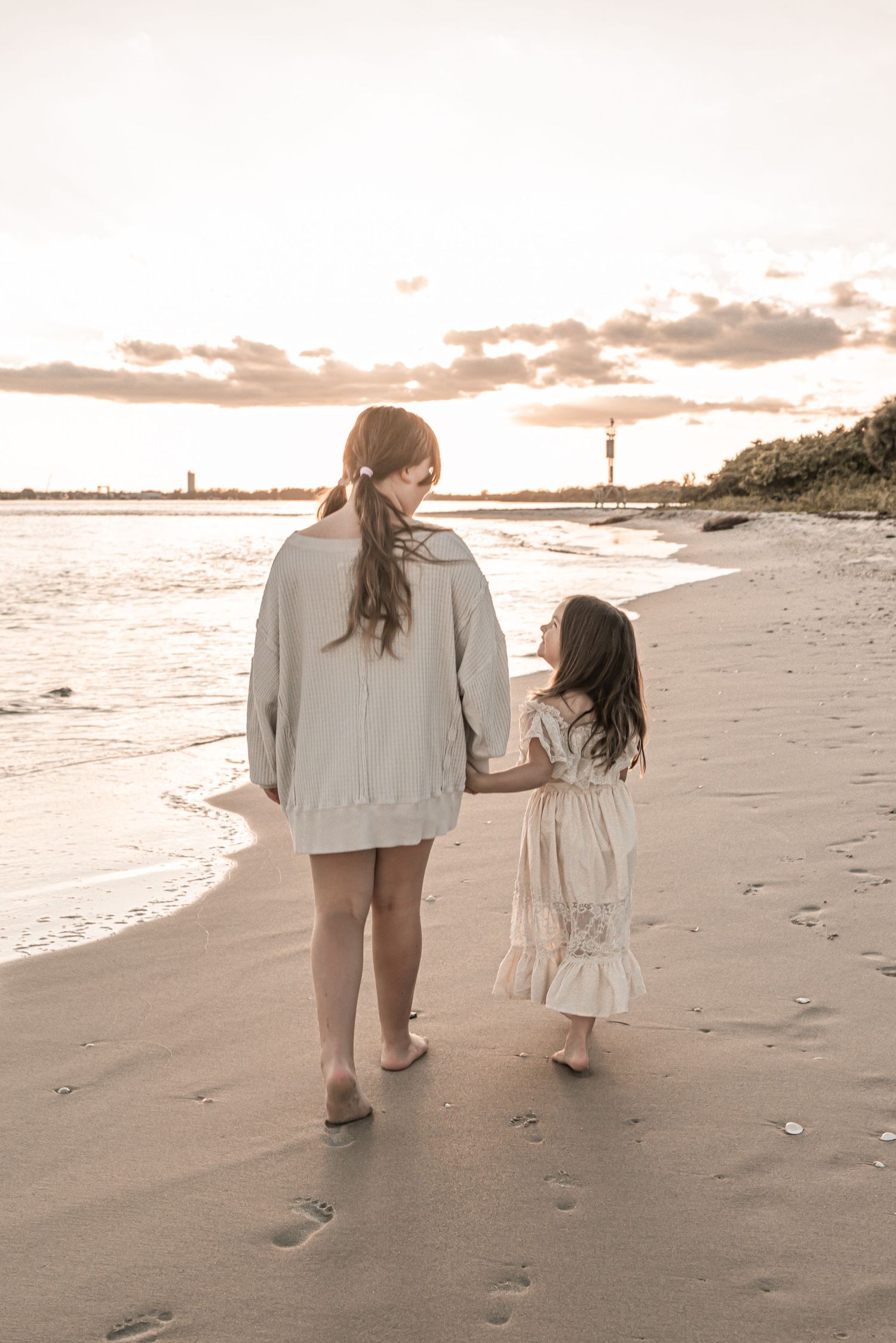 A parent and child walk hand in hand along a beach at sunset leaving footprints in the sand.