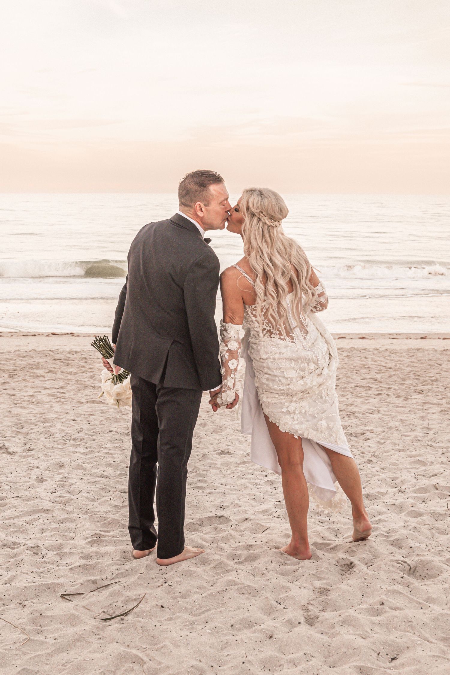 Couple walking playfully along the beach at sunset in formal wedding attire.