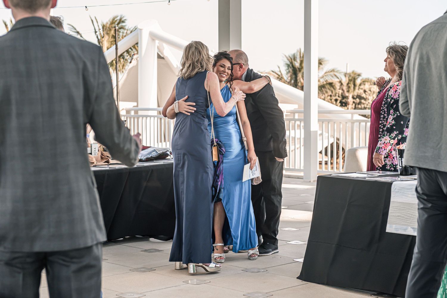 People gather at an outdoor reception with black tables and white columns in the background.